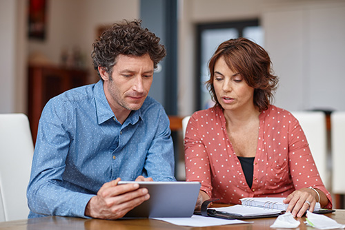 blogPost_parents Comparing student loans. A man and woman sit next to each other looking at papers and a tablet the man is holding.